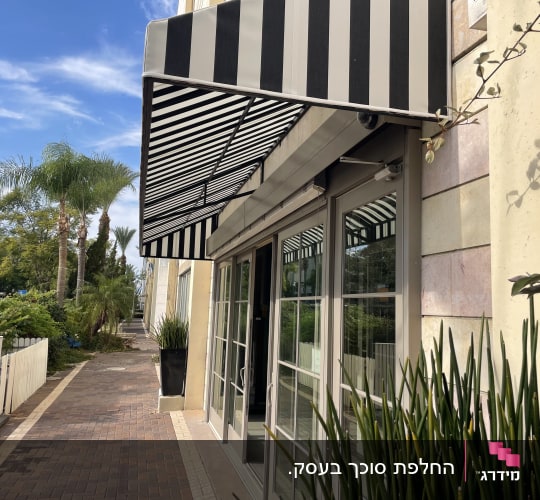 סוכך מפוספס מעל חלון בניין עם צמחייה מסביב